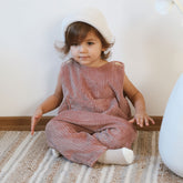 Toddler wearing dusty pink corduroy overalls and a beanie sitting on floor